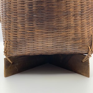 May include: A woven brown wicker basket with a wooden base. The basket is made of natural materials and has a rustic look.
