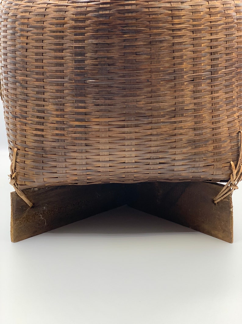 May include: A woven brown wicker basket with a wooden base. The basket is made of natural materials and has a rustic look.