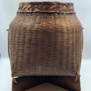 May include: A large, brown woven basket with a triangular wooden base. The basket is made of natural materials and has a woven pattern.