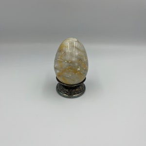 May include: A white and yellow marble egg on a silver stand with an ornate design.