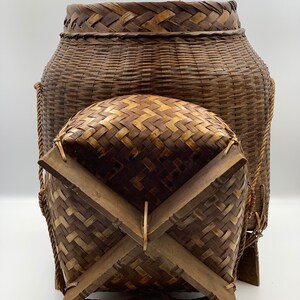 May include: A large, woven, brown basket with a lid and four wooden legs. The basket is made of natural materials and has a rustic appearance.