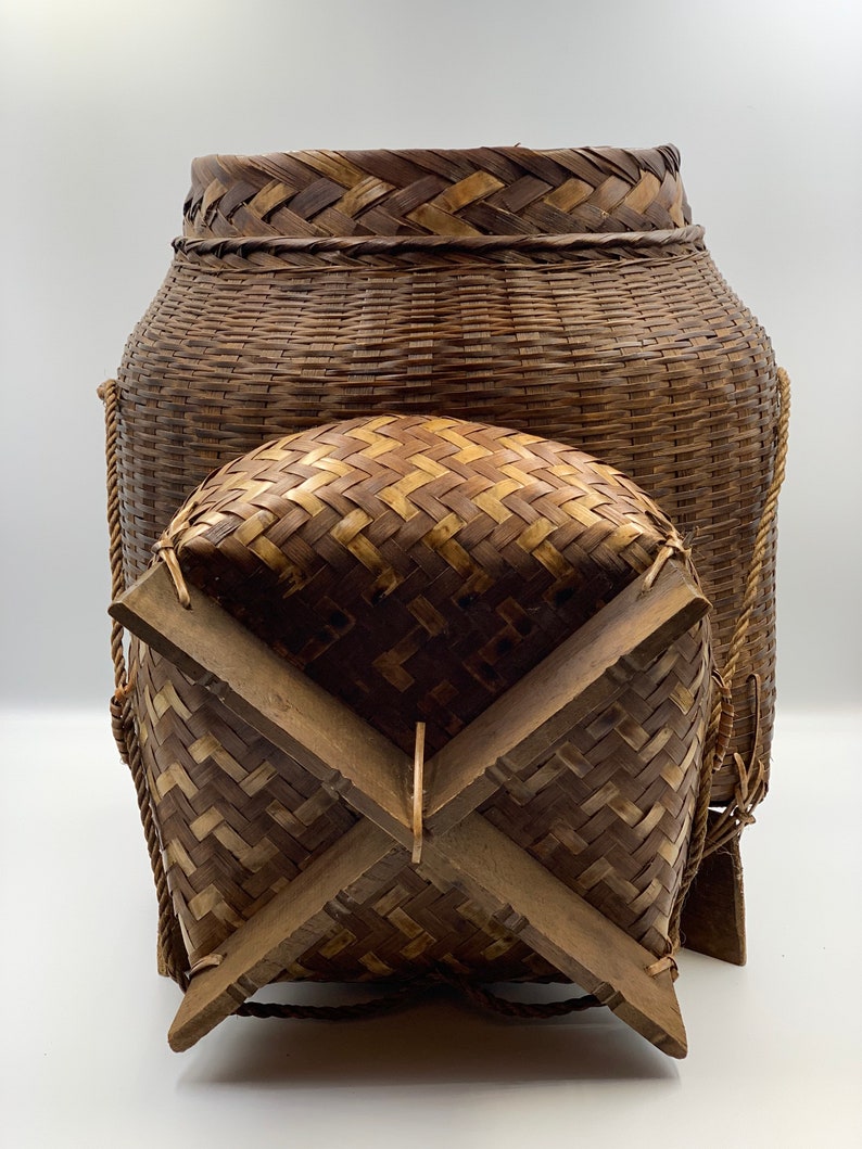 May include: A large, woven, brown basket with a lid and four wooden legs. The basket is made of natural materials and has a rustic appearance.