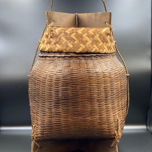 May include: A brown woven basket with a wooden top and a rope handle. The basket is sitting on a wooden stand.