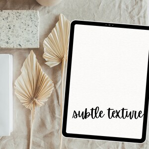 May include: A white tablet with a black border and the text "subtle texture" on the screen. The tablet is on a beige surface with dried palm leaves.