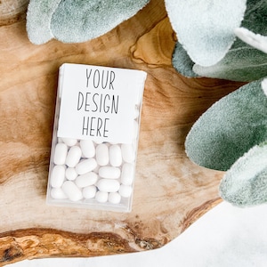 May include: A clear plastic container filled with white mints. The container has a white label with the text "YOUR DESIGN HERE" printed on it. The container is sitting on a wooden surface.