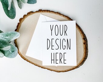 Puede incluir: Una tarjeta blanca con el texto "YOUR DESIGN HERE" sobre una rodaja de madera. La tarjeta está encima de un sobre blanco.