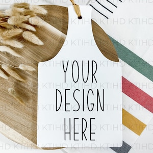 Może przedstawiać: Biała ceramiczna tabliczka kuchenna z pętlą do zawieszenia. Tabliczka ma czarny tekst, który brzmi "YOUR DESIGN HERE". Tabliczka leży na drewnianej desce do krojenia z wiązką suszonej trawy pampasowej.