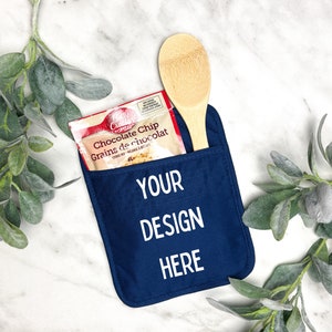 May include: A blue pot holder with a pocket for a wooden spoon and a packet of chocolate chips. The pot holder has the text "YOUR DESIGN HERE" printed on it.