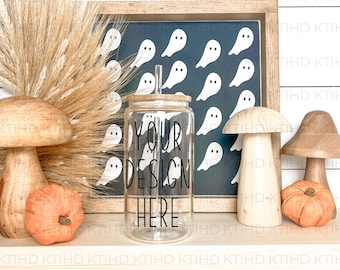 May include: A clear glass tumbler with a wooden lid and straw. The tumbler has the text "Your Design Here" written on it. The tumbler is sitting on a white shelf with a wooden mushroom, a small orange pumpkin, and a framed sign with a blue background and white ghost silhouettes.