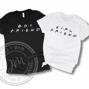 May include: Two t-shirts, one black and one white, with the words "BOY FRIEND" and "GIRL FRIEND" printed on them in a stylised font with colourful dots.