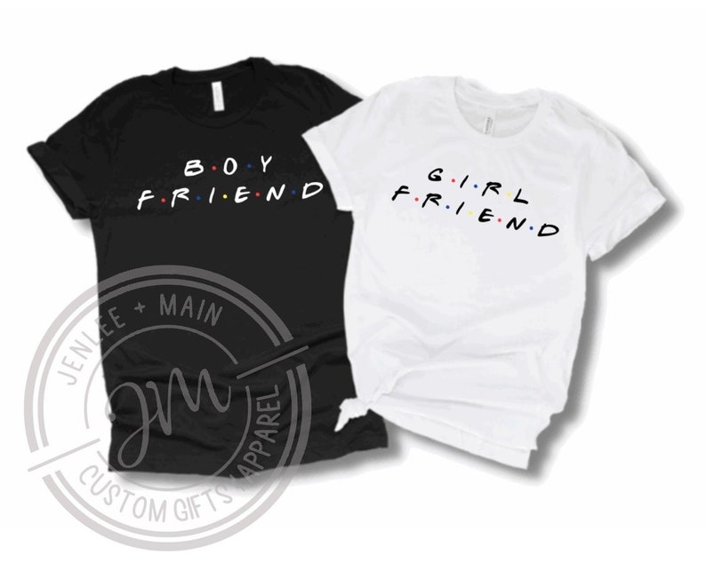 May include: Two t-shirts, one black and one white, with the words "BOY FRIEND" and "GIRL FRIEND" printed on them in a stylised font with colourful dots.