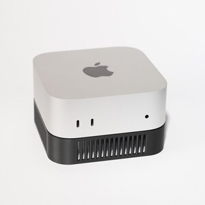 May include: Silver and black desktop computer with the Apple logo on top. The device has a square shape with rounded corners. The bottom section is black with ventilation slots.