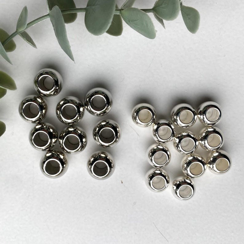 May include: A close-up of two groups of silver metal beads with a hole in the centre of each bead. The beads are arranged in a circular pattern.