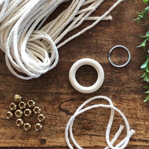 May include: A collection of crafting supplies including white cotton rope, wooden rings, gold beads, and a metal ring.