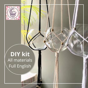 May include: DIY kit for making macrame plant hangers. The kit includes three different coloured cords: black, white, and natural. Each cord is strung with gold beads and attached to a glass globe.