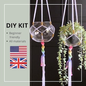 Puede incluir: Dos terrarios colgantes de cristal con red de macramé blanca y borlas de colores arcoíris. Un terrario está vacío y el otro contiene vegetación. La imagen incluye el texto "DIY KIT" y las banderas de Estados Unidos y Reino Unido.