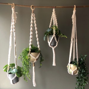 Può includere: Quattro portavasi in macramè con diverse piante in vaso. I portavasi sono realizzati in cordoncino di cotone bianco e hanno un design semplice. Le piante sono una varietà di fogliame verde.
