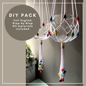 May include: DIY pack of two macrame plant hangers with glass globes. The hangers are white with rainbow colored beads and tassels. The text "DIY PACK Full English Step-by-Step All materials included" is on the image.