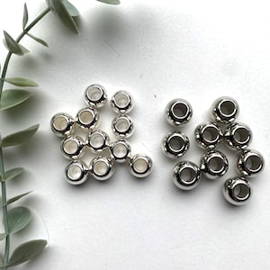 May include: A set of silver metal beads with a hole in the centre. There are two groups of beads, one group of 15 beads and another group of 10 beads.