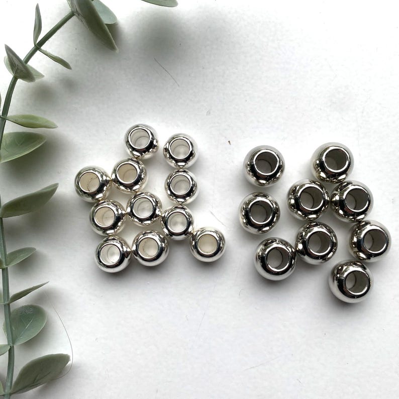 May include: A set of silver metal beads with a hole in the centre. There are two groups of beads, one group of 15 beads and another group of 10 beads.