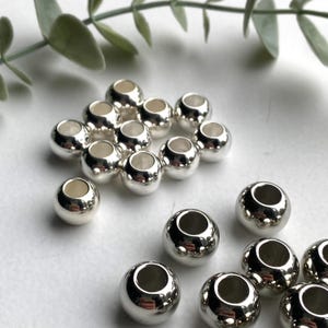May include: A group of silver-toned metal beads with a hole in the centre. The beads are arranged in a circular pattern on a white surface.