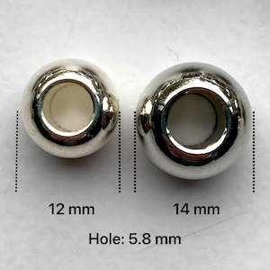 May include: Two silver metal beads with a hole in the centre. The bead on the left is 12 mm in diameter and the bead on the right is 14 mm in diameter. The hole in each bead is 5.8 mm in diameter.