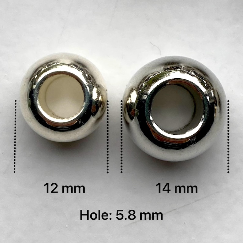 May include: Two silver metal beads with a hole in the centre. The bead on the left is 12 mm in diameter and the bead on the right is 14 mm in diameter. The hole in each bead is 5.8 mm in diameter.