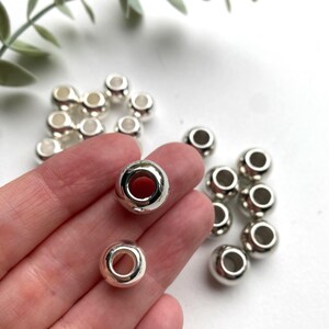 May include: A close-up of silver metal beads with a hole in the centre. The beads are round and smooth.