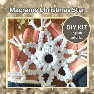May include: A white macrame Christmas star with gold embellishments. The star is displayed in open hands, highlighting the detailed knotwork. The image includes the text "Macrame Christmas Star" and "DIY KIT English tutorial".