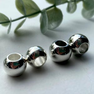 May include: Four silver metal beads with a hole through the centre. The beads are round and shiny.