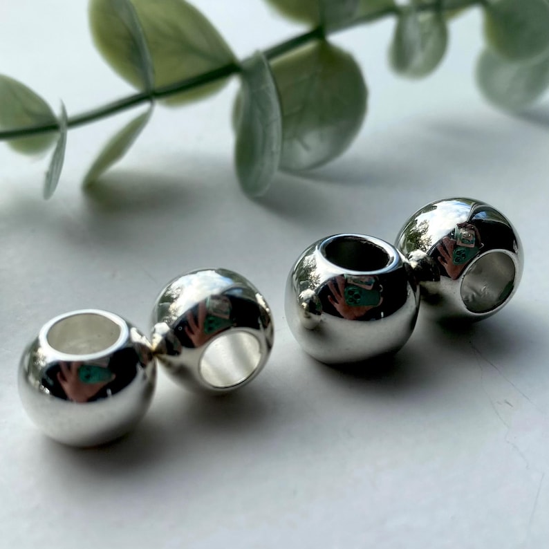 May include: Four silver metal beads with a hole through the centre. The beads are round and shiny.