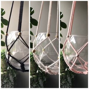 May include: Three macrame plant hangers with glass globes. The hangers are made with black, white, and pink cord and have gold beads.