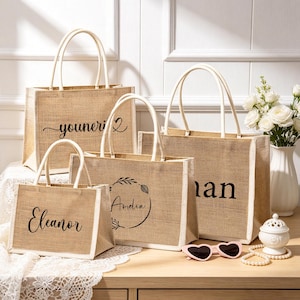 Puede incluir: Cuatro bolsas de yute rectangulares con asas blancas y texto en negro. Las bolsas presentan los nombres Eleanor, Amelia y otros impresos en varias fuentes. Las bolsas est&aacute;n dispuestas en grupo, mostrando diferentes tama&ntilde;os y dise&ntilde;os.