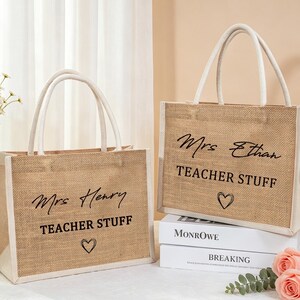 Pu&ograve; includere: Due borse rettangolari in juta con bordi e manici in tessuto bianco. Ogni borsa presenta una scritta nera "Mrs Henry" o "Mrs Ethan" sopra le parole "TEACHER STUFF" e un piccolo cuore disegnato a mano nella parte inferiore.