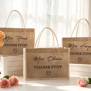 Pu&ograve; includere: Tre borse rettangolari in juta con manici bianchi. Ogni borsa presenta una scritta nera che riporta "Mrs. Noah", "Mrs. Olivia" o "Mrs. Faye" sopra le parole "TEACHER STUFF" e un piccolo contorno di cuore disegnato a mano.