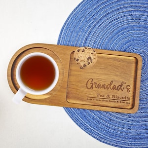 Może przedstawiać: Drewniana taca do serwowania z filiżanką herbaty i ciasteczkiem. Taca jest grawerowana tekstem "Granddad's Tea & Biscuits Lots of love from Smith & Kim xxx".