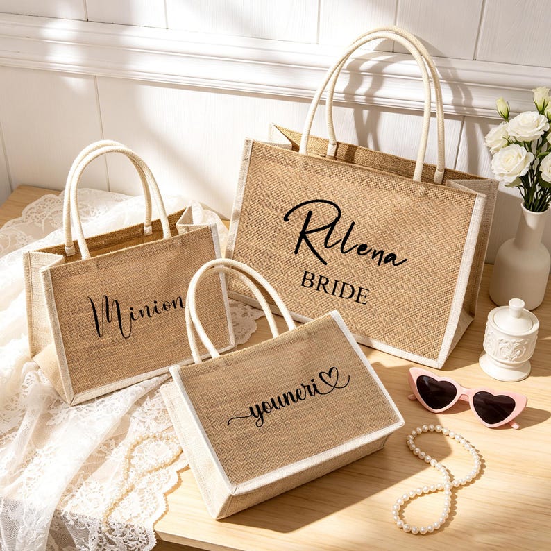 Puede incluir: Tres bolsos de yute rectangulares con bordes y asas blancas. El bolso m&aacute;s grande presenta el texto negro "Rllena BRIDE". Un bolso m&aacute;s peque&ntilde;o muestra el texto negro "Minion" y el otro el texto negro "youneri" junto a un coraz&oacute;n.