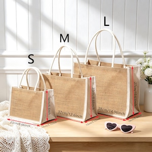 Puede incluir: Tres bolsos de yute rectangulares en tama&ntilde;os peque&ntilde;o, mediano y grande con bordes y asas blancas. El bolso peque&ntilde;o mide 22 cm de ancho por 16 cm de alto, el mediano 32 cm por 22 cm, y el grande 38 cm por 27 cm.