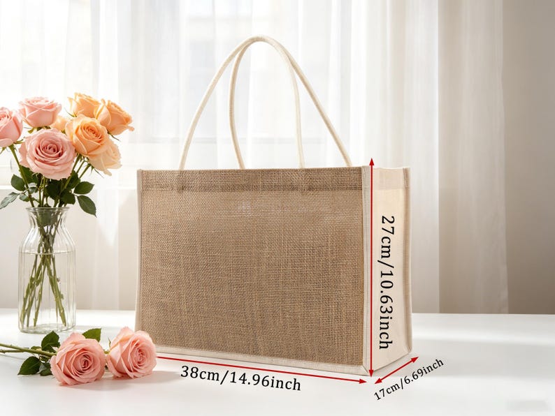 Pu&ograve; includere: Una borsa tote rettangolare in juta con pannelli laterali in tessuto bianco e due manici superiori bianchi. La borsa misura 38 cm di larghezza, 27 cm di altezza e 17 cm di profondit&agrave;, come indicato dalle frecce di misurazione rosse.