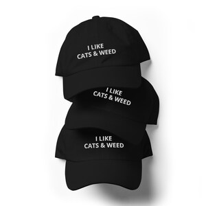 May include: Three black baseball caps stacked on top of each other. Each cap has white embroidery that reads "I LIKE CATS & WEED".