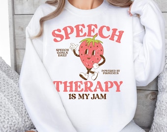 May include: White sweatshirt with a retro design featuring the words "SPEECH THERAPY IS MY JAM" in pink. A smiling strawberry character is in the center. The sweatshirt also includes the phrases "SPEECH GOALS DAILY" and "POWERED BY PHONEMES".