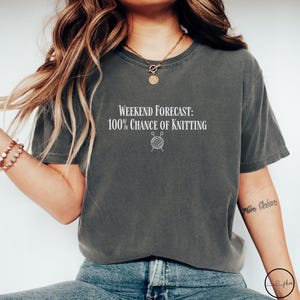 May include: A gray t-shirt with the text "Weekend Forecast: 100% Chance of Knitting" and a small illustration of yarn and knitting needles.