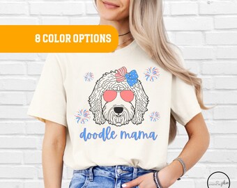 May include: A white t-shirt with a doodle dog wearing sunglasses and a red, white, and blue bow. The text "doodle mama" is printed in blue below the dog.