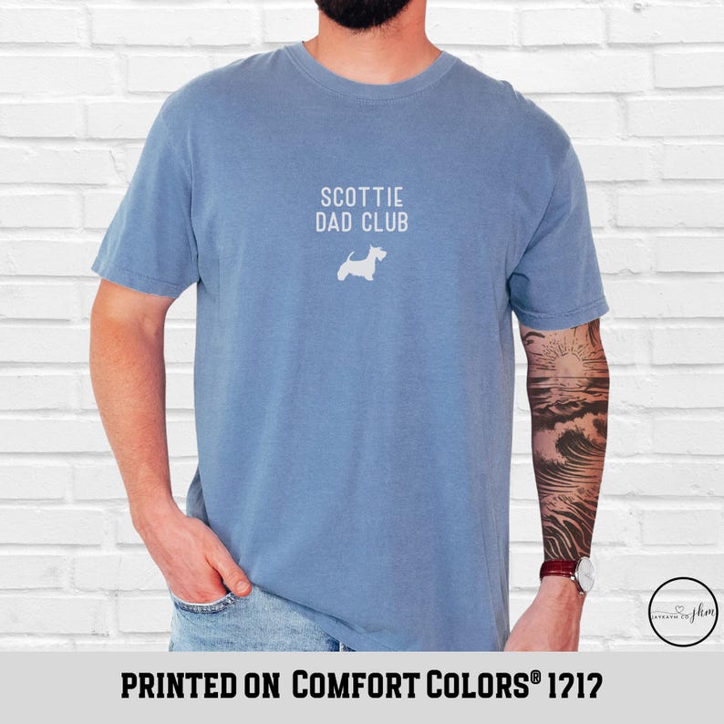 May include: A blue t-shirt with the text "SCOTTIE DAD CLUB" and a white silhouette of a Scottish Terrier. The shirt is printed on Comfort Colors 1212 fabric.