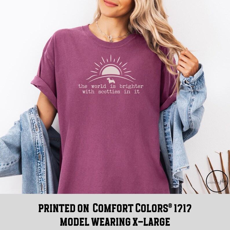 May include: A maroon t-shirt with the text "the world is brighter with scotties in it" and a graphic of a sun and a dog. The shirt is a Comfort Colors 1212, and the model is wearing an X-Large.