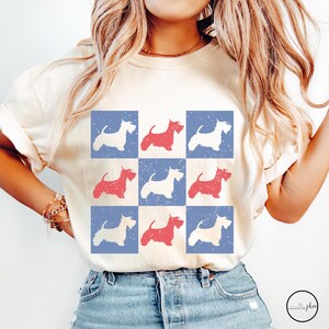 May include: A white t-shirt with a blue and white checkered pattern featuring red and white silhouettes of Scottish Terriers.
