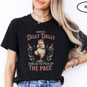 May include: Black t-shirt featuring a cartoon capybara doing yoga with the text "Born to Dilly Dally Forced to Pick Up The Pace".