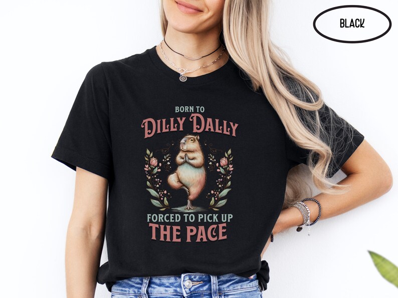 May include: Black t-shirt featuring a cartoon capybara doing yoga with the text "Born to Dilly Dally Forced to Pick Up The Pace".