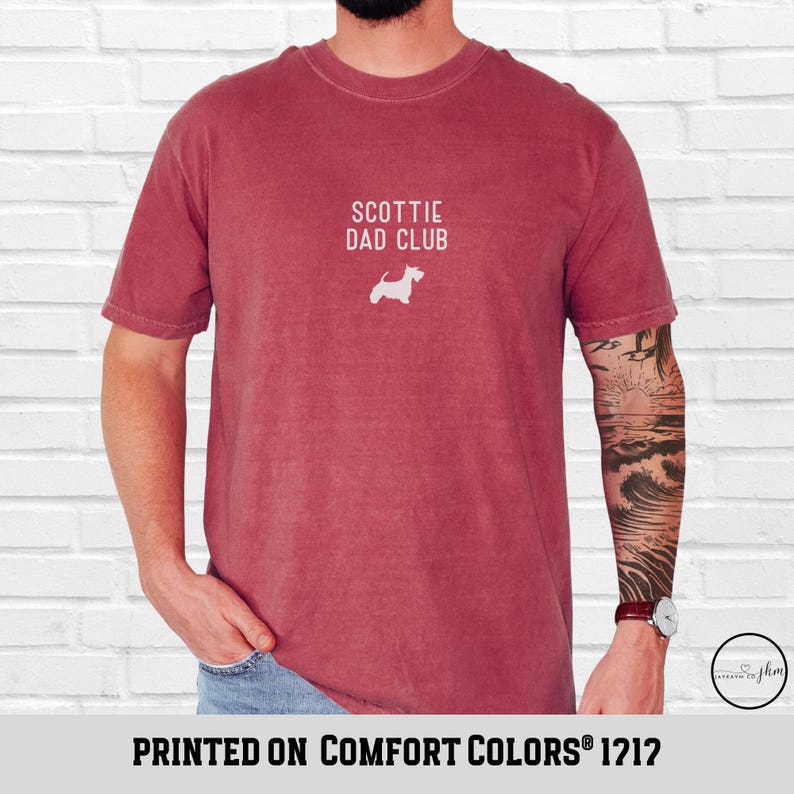 May include: A maroon t-shirt with the text "SCOTTIE DAD CLUB" and a white silhouette of a Scottish Terrier. The phrase "PRINTED ON COMFORT COLORS 1212" is printed at the bottom of the shirt.