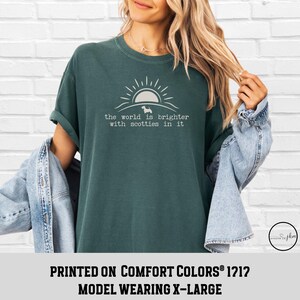 May include: Dark teal t-shirt with the text "the world is brighter with scotties in it" in white. The design includes a sun and a silhouette of a dog. The shirt is a Comfort Colors 1212 model, size X-Large.